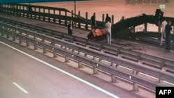 Într-o imagine distribuită de SBU se văd persoane care inspectează daunele provocate podului Kerci, marți dimineață.