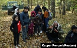 Un grup de migranți irakieni, înconjurat de polițiști de frontieră și ofițeri de poliție după ce au trecut frontiera bielorusă-poloneză la Hajnowka, 14 octombrie 2021.