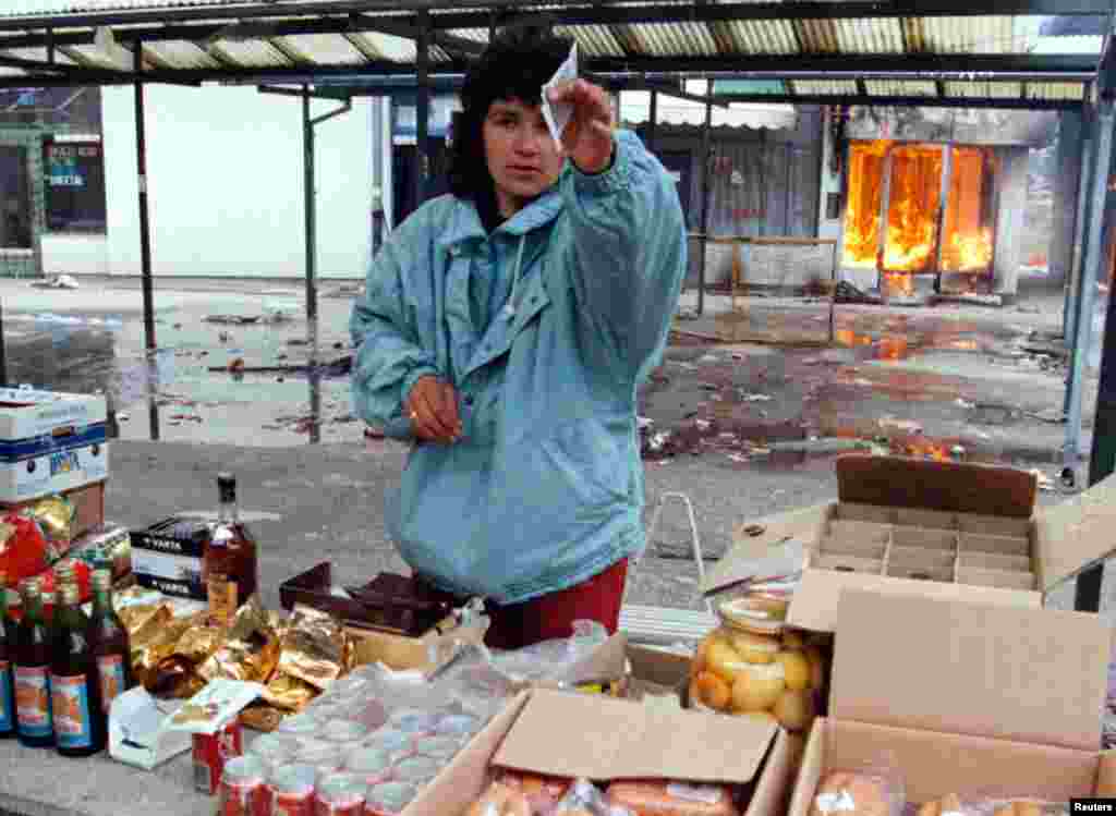 A Serb woman sells goods in a market as a shop burns behind her in Ilidzia, a Serb-held suburb of Sarajevo on March 9, 1996, three days before it was due to come under Croat and Muslim rule.