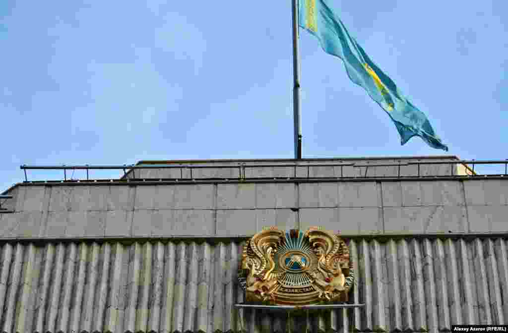 2018 жылы 28 маусымда Қазақстанда кейбір конституциялық заңдарға өзгертулер мен толықтырулар енгізу туралы заң қабылданды. Мысалы, "Қазақстан Республикасының мемлекеттік рәміздері" туралы заңға өзгерістер енгізіліп, 1 қарашадан бастап Қазақстан елтаңбасындағы "Қазақстан" жазуы "Qazaqstan" деп жазылатын болды. Алайда, мемлекеттік органдар ғимаратының сыртына ілінген елтаңбаларға қарап, латын қарпіндегі жаңа жазуға көшу барлық жерде бірдей емес екенін байқауға болады. 2019 жылы 27 наурызда түсірілген фотодағы Алматы қаласы әкімдігінің сыртына ілінген елтаңбадағы мемлекет атауы кириллица әріптерімен жазылған.