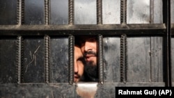 دو زندانی محبس ننگرهار از دروازه زندان بیرون را نگاه می‌کنند.