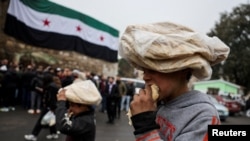 Fëmijët hanë bukë në një rrugë pranë një flamuri të adoptuar nga liderët e rinj sirianë, pas rrëzimit të Bashar al-Assad të Sirisë, në Damask, Siri, 24 dhjetor 2024.