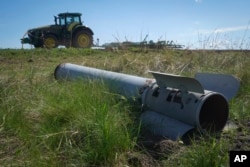 A fragment of a Russian missile lies in a field as a farmer works his land in Ukraine's war-torn Kharkiv region.