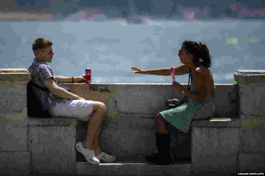 Dvoje mladih osvježavaju se pićem i sladoledom pored rijeke Tagus, u Lisabonu, 29. juna.