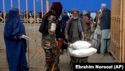 د طالبانو یو حکومتي سرتېری په کابل کې په اړمنو خلکو کې د خوراکي مرستو وېش مرکز مخې ته پهره کوي - پخوانی انځور.