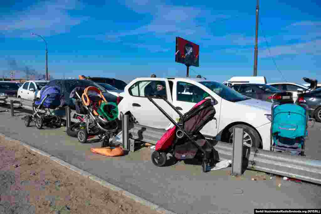 Дарога перад разбураным Раманаўскім мостам. Тут падчас эвакуацыі людзі пакідалі свае машыны, вазкі, іншыя рэчы, якія не маглі ўзяць з сабой. Шмат машынаў тут згарыць у выніку расейскіх абстрэлаў.Зьлева фота 11 сакавіка 2022 году, справа — з сакавіка 2025 году