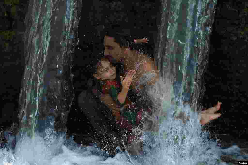 Пешавардагы мээ кайнаткан ысыктан качып, баласы менен каналдагы сууга түшкөн киши. Пакистан.