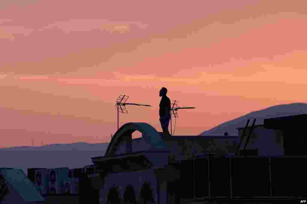 Тегерандагы имараттын үстүндө тынымсыз бомбалоо менен батып бараткан күндү карап турган эркек. 