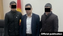 Шектүү кармалган учур. УКМК кызматкерлеринин ортосунда турат. Сүрөт атайын кызматтыкы. 