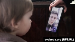 Ihar Losik's wife, Darya Losik, shows a photo of him to their young daughter in January 2023.
