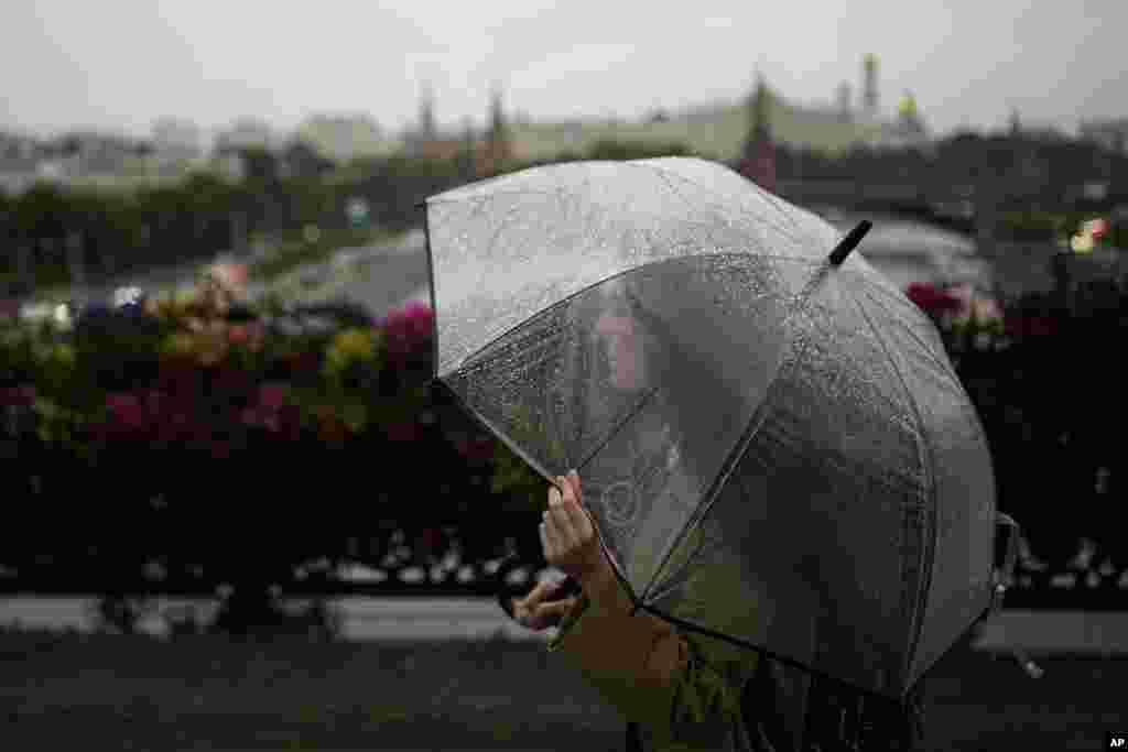 Женщина переходит по пешеходному мосту через Патриаршие, держа в руках прозрачный зонт, в дождливый день в Москве, Россия, 30 июня 2025 года, на фоне Кремля. AP Photo/Pavel Bednyakov