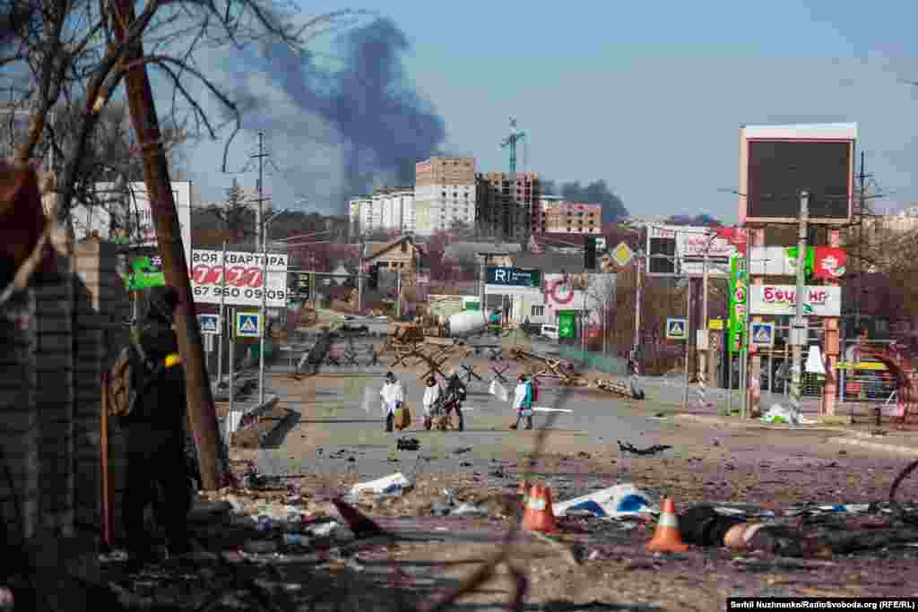 Людзі пешшу, прыкрываючыся белым, пакідаюць Бучу.Зьлева фота 11 сакавіка 2022 году, справа — з сакавіка 2025 году