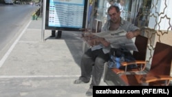 Awtobus duralgasynda gazet okap oturan bir adam (arhiw suraty)