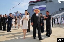 Kim Jong-un și fiica sa, Ju-ae (în stânga), la ceremonia celei de-a doua lansări a distrugătorului „Choe Hyon” în portul orașului Rason. Cu o lună înainte, nava fusese avariată în urma unei lansări eșuate, fiind lansată cu succes abia la a doua încercare, pe 12 iunie 2025.