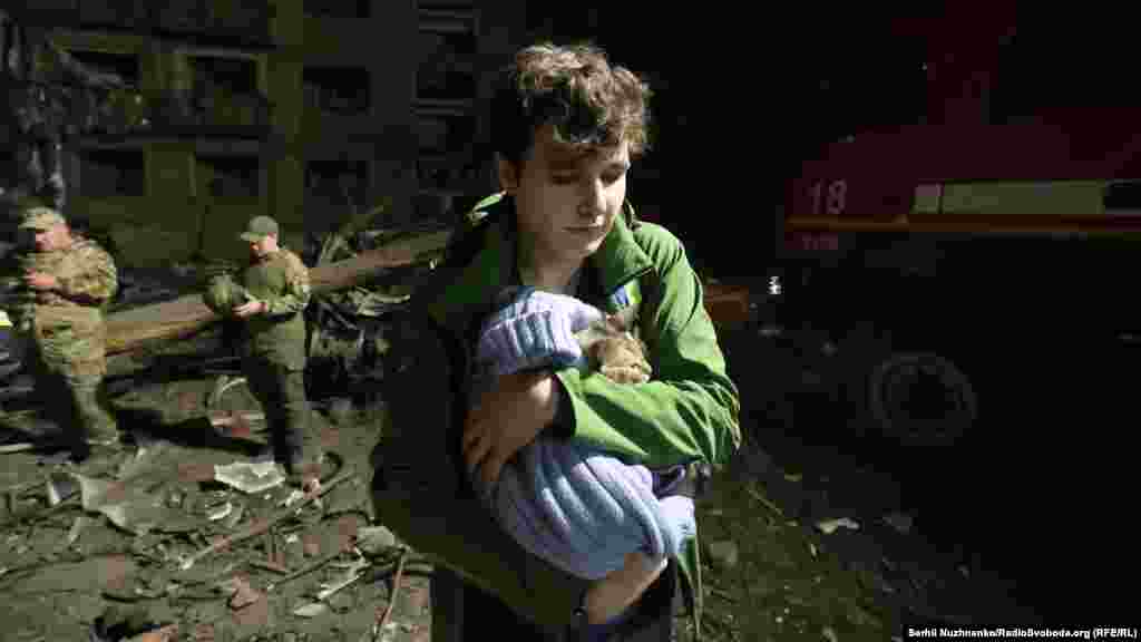 Një djalë mban një mace në duar duke dalë nga rrënojat e një ndërtese banimi që u godit nga një sulm me raketë ruse në një qark të Kievit.