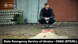 În această imagine publicată de serviciile de urgență ale Ucrainei, un bărbat stă cu chipiul în mână lângă corpul neînsuflețit al unei femei ucise de o dronă rusească, în regiunea Kiev, pe 18 mai 2025 