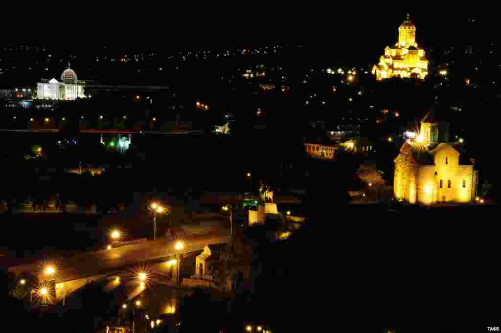 A nighttime view of the 13th century Metekhi Church (front right), the Holy Trinity Cathedral (back right), and the Presidential Palace (far left).