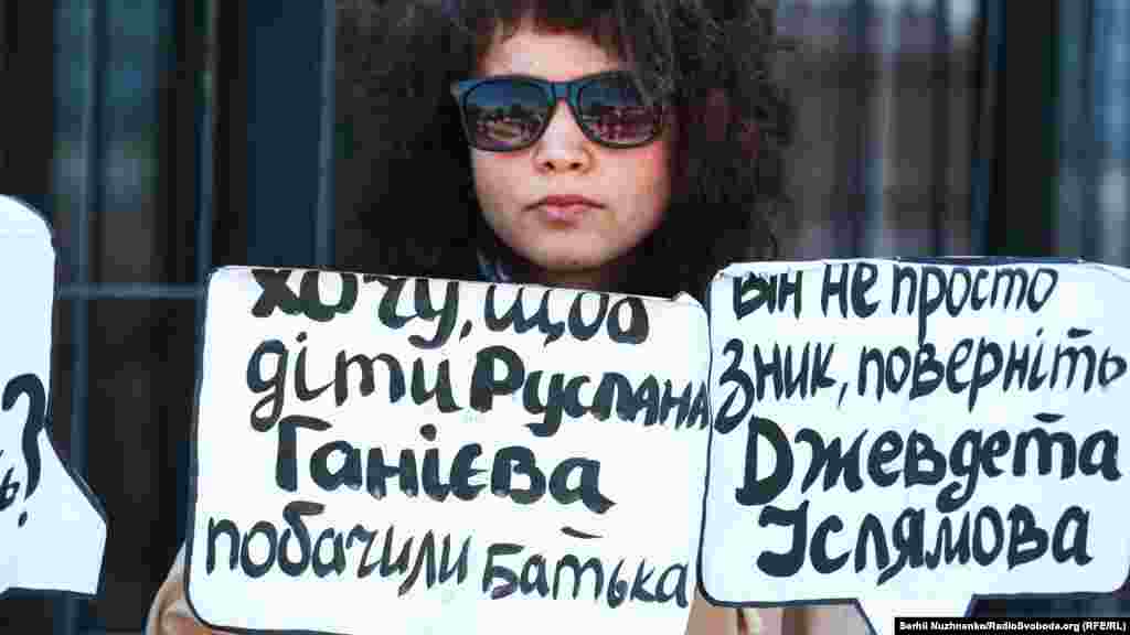 Bu qız qolunda Qırımda ğayıp olğanlardan Ruslan Ganiyev ve Cevdet İslâmovnıñ adları ile levhalarnı tuta