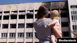 Мама з дитиною біля будівлі в Маріуполі, пошкодженої внаслідок обстрілу реактивними системами залпового вогню з боку російсько-сепаратистських сил у 2015 році