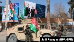 Ýol gözegçiligini amala aşyrýan owgan howpsuzlyk wekili Owganystanyň we Türkmenistanyň prezidentleriniň suratynyň fonunda, TOPH-yň Hyratda düýbüniň tutulmagynyň öňüsyrasynda, Owganystan 