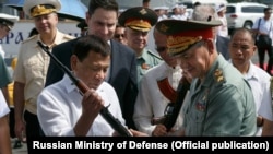 ფილიპინების ყოფილი პრეზიდენტი როდრიგო დუტერტე (მარცხნივ) ამოწმებს რუსეთის მიერ მიწოდებული ავტომატების დიდ პარტიას რუსეთის თავდაცვის ყოფილ მინისტრ სერგეი შოიგუსთან ერთად. მანილის პორტი, 2017 წლის 25 ოქტომბერი.