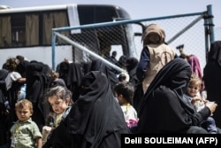 Siriýanyň demirgazyk-gündogaryndaky al-Hol lagerindäki awtobusyň öňünde duran aýallar bilen çagalar. 2019-njy ýylyň 3-nji iýuny.