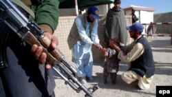 په چمن کې یو واکسیناتور ماشوم ته د پولیو څاڅکي ورکوي او د امنیت یو ساتونکی هم هلته ولاړ دی - انځور له ارشیفه 