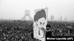 დემონსტრანტებს აღმართული აქვთ გადასახლებული ისლამური ლიდერის, აიათოლა რუჰოლა ხომეინის პოსტერი. შაჰის საწინააღმდეგო ეს დემონსტრაცია 1978 წლის 10 დეკემბერს გაიმართა, შაიას მონუმენტთან, რომელიც მონარქის პატივსაცემად აშენდა.