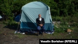 Мъж седи пред палатката, в която живее