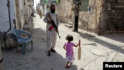 A girl with a cricket bat walks past a militant in Rahim Yar Khan, southern Punjab Province (file photo)
