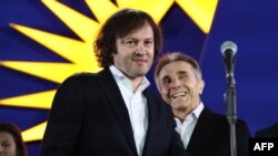 „ქართული ოცნების“ ლიდერები, ირაკლი კობახიძე (მარცხნივ) და ბიძინა ივანიშვილი პარტიისა და ევროკავშირის დროშის ფონზე