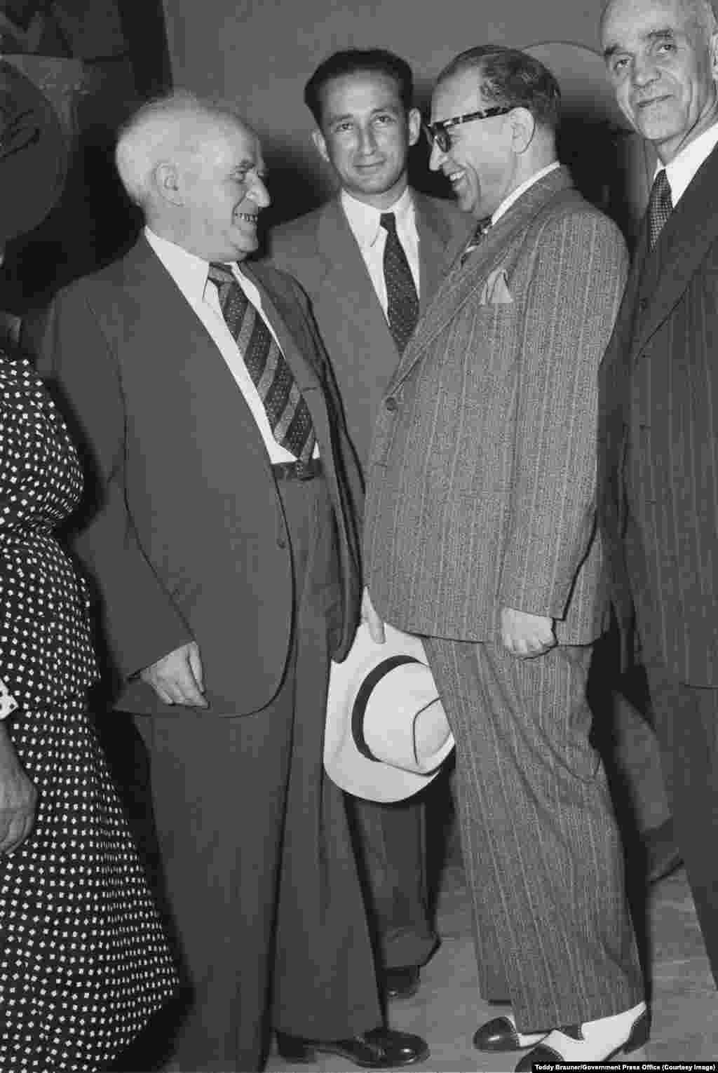 Исроилнинг илк бош вазири Давид Бен Гурион (чапда) 1950 йили Қуддусда Эрон делегацияси томонидан ўтказилган қабул маросимида эронлик дипломат Ризо Саффиния (йўл-йўл костюмда) билан учрашяпти.Кейинчалик Теҳрон ва Тель-Авив ўртасида кунлик авиақатновлар амалга оширилади. Қолаверса, Эрон ва Исроил яширин равишда қўшма ракеталар тизимини ишлаб чиқиш устида ҳам ҳамкорлик қилишган.