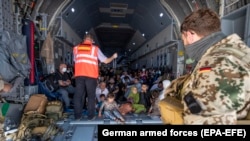 Un membru al staff-ului aeronavei informează evacuații din Afganistan, aflați la bordul unui avion de transport A400 al Forțelor Aeriene Germane, la sosirea pe aeroportul din Tașkent/Uzbekistan - 19 august 2021
