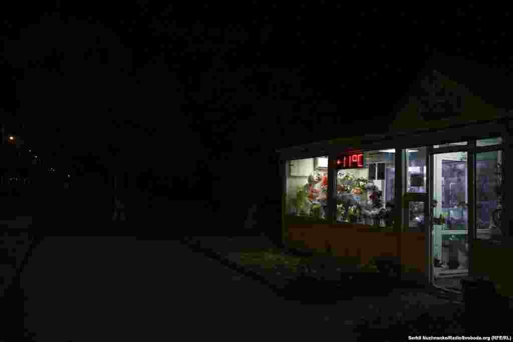 Асьветленая кветкавая крамка сярод амаль поўнай цемры на Паркавай вуліцы ў Краматорску