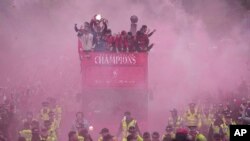 Echipa de fotbal Liverpool, într-un autobuz decapotabil în centrul orașului, demonstrând mulțimii trofeul din Premier League