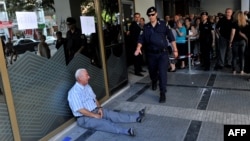 A man sits on the sidewalk crying outside a national bank branch as pensioners queue to withdraw their pensions, with a limit of 120 euros, in Thessaloniki.