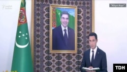 Serdar Berdimuhamdow kakasy Gyrbanguly Berdimuhamedowyň portretiniň öňünde durup, oňa hasabat berýär. 