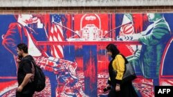 Маж и жена поминуваат крај мурал насликан на фасадата на поранешната американска амбасада во Техеран, на кој е прикажан ирански службеник во цивил како седи наспроти американски службеник во воена облека 