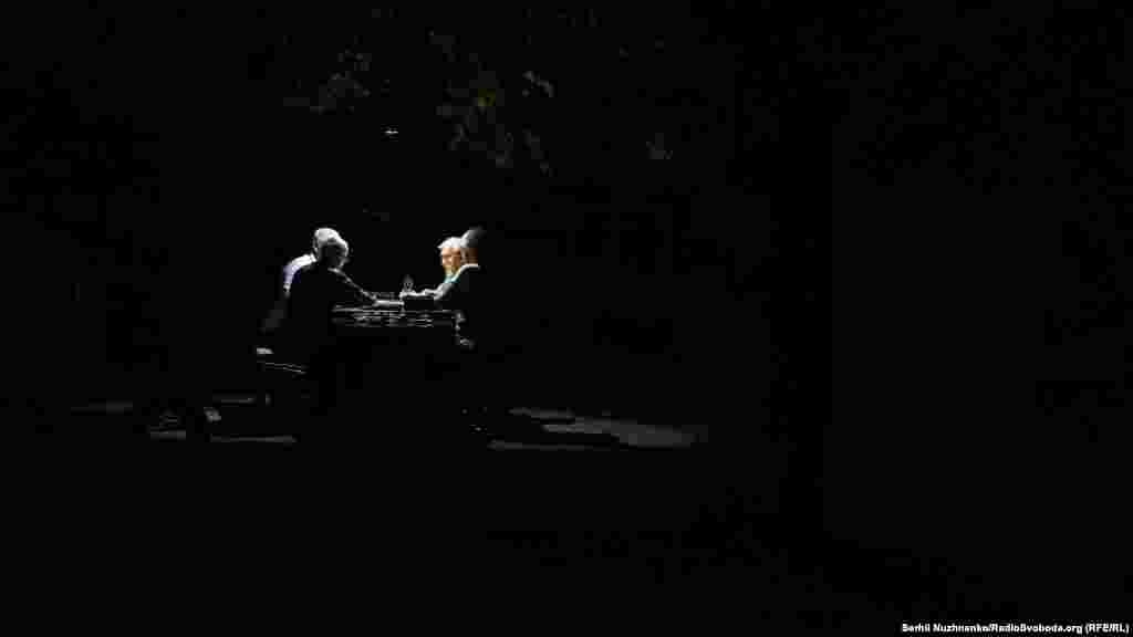 Мужчыны гуляюць у даміно пры сьвятле ліхтарыка