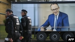 Polițiști trecând pe lângă un panou electoral al liderului CDU, Friedrich Merz, la Oberhausen, în vestul Germaniei, la 21 februarie.