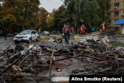 Ukrainian municipal service workers clean up debris near buildings damaged during Russian drone and missile strikes in the town of Brovary, outside of Kyiv, October 10, 2025.
