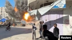 په غزه کې د اسراییلو تر برید وروسته یوې ودانۍ اور اخیستی دی او یوشمېر کسان د پېښې له ځای سره نېږدې ولاړ دي - د مارچ ۲۳مې انځور. 