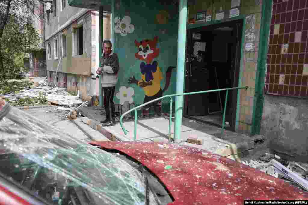 Un bărbat stă în fața scării blocului său, avariat în urma unui bombardament. Pe peretele din spate este desenat Motanul Leopold - unul dintre personajele clasice din desenele animate sovietice.