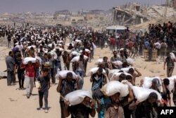 Oameni cară saci de făină livrați după ce camioanele care transportau ajutoare umanitare au intrat în nordul Gazei pe 27 iulie 2025, venind de la punctul de trecere a frontierei Zikim.