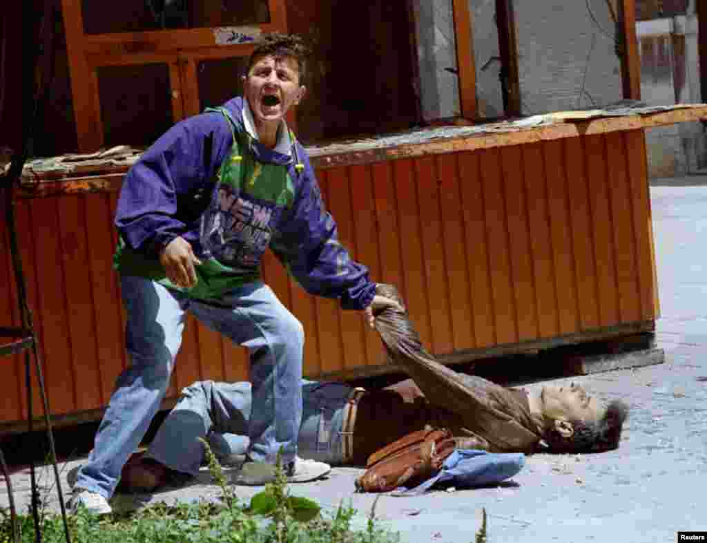 A man calls for help for one of the casualties of a mortar explosion.