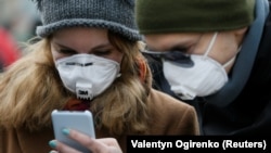 Луѓе со маски против ковид19 гледаат во своите мобилни телефони